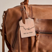 A close-up of a brown leather bag with a hanging wooden tag engraved with the words 'we WE THE FREE'.