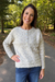 A woman smiling outdoors on a paved path wearing a cream cable-knit long-sleeve henley sweater with blue jeans.