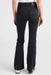 Rear view of a person wearing black flared jeans with a white top and white sneakers, photographed against a light gray studio background.