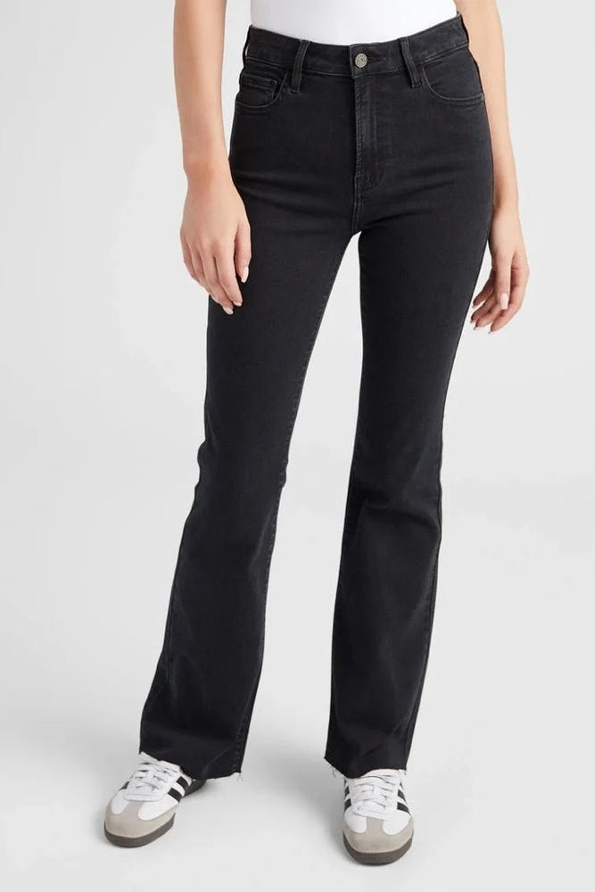 A model wearing a pair of black high-rise flare jeans with white sneakers, shown from the waist down against a light gray studio background.