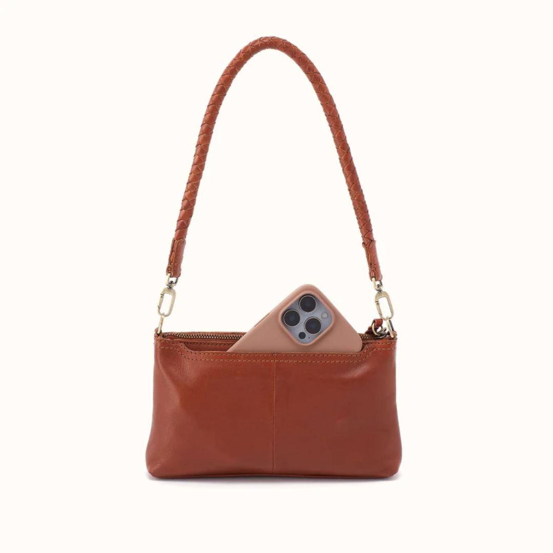 A brown leather shoulder bag with a braided strap and gold-tone hardware, shown with a smartphone tucked into its zippered pocket against a plain off-white background.
