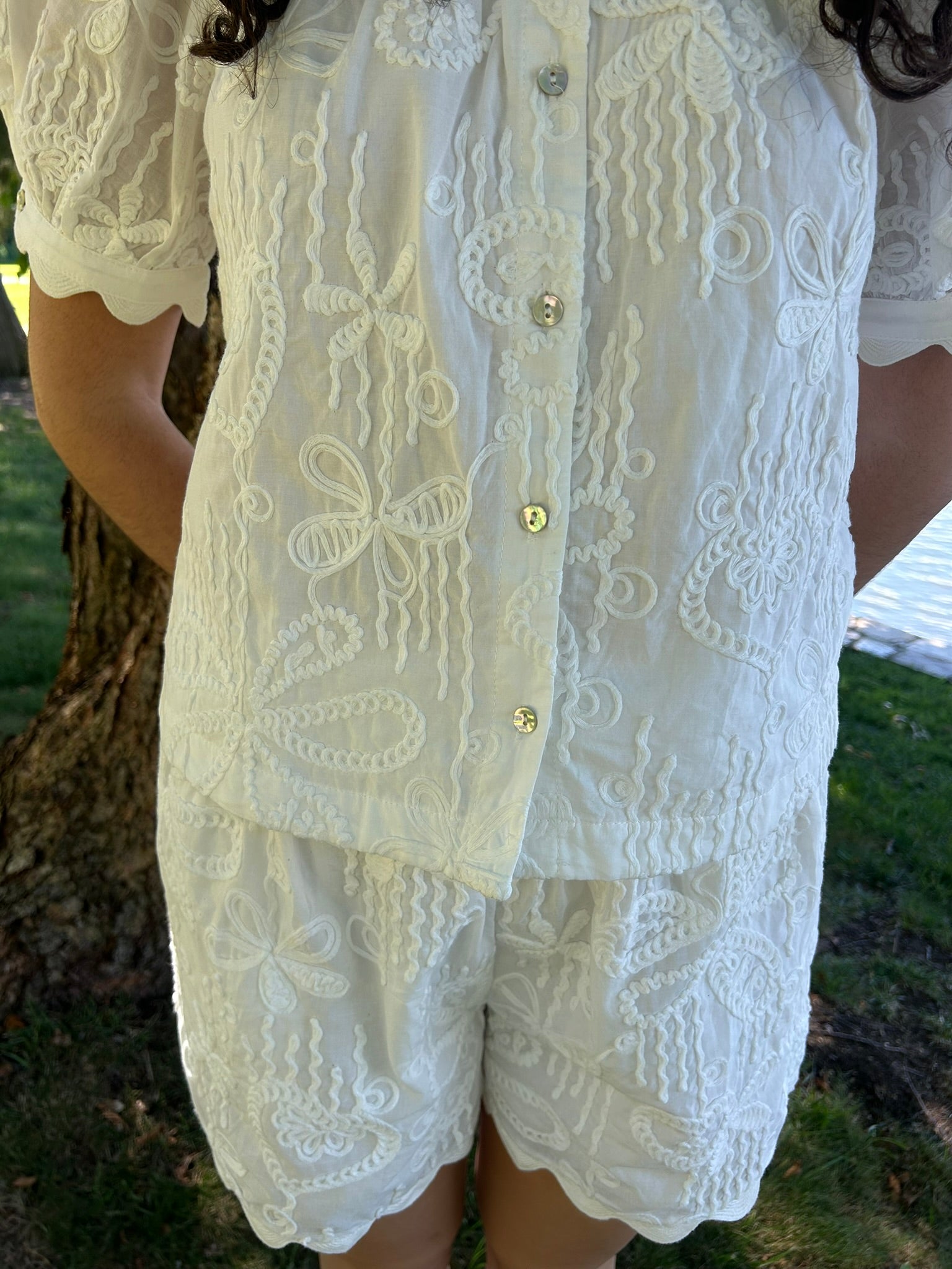 White lace set with gold buttons worn by a person outdoors.