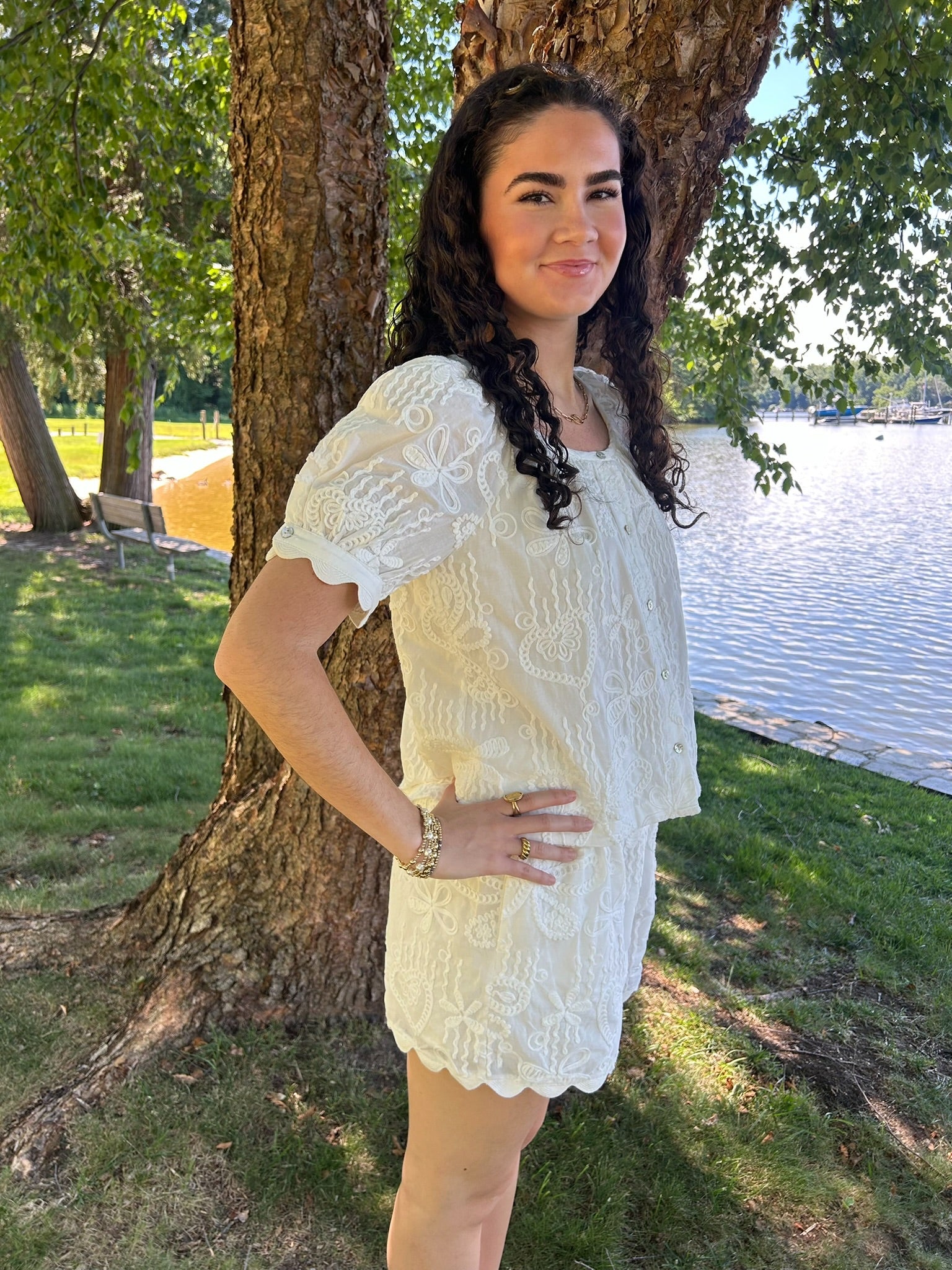 Woman in a white set standing by a tree by a lake