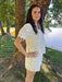 Woman in a white set standing by a tree by a lake