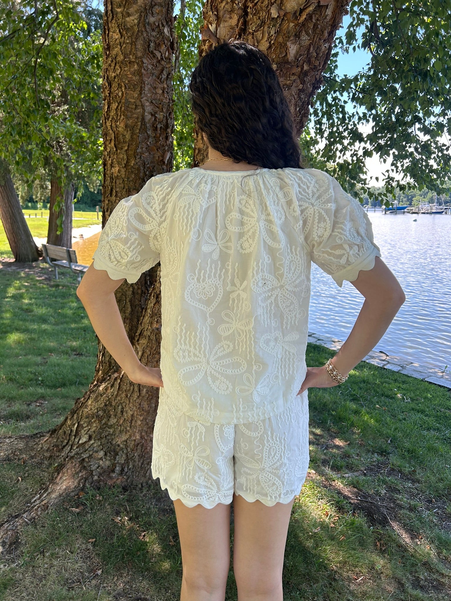 Person wearing a white lace outfit by a tree and body of water