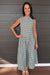 A woman modeling a sleeveless green and white gingham midi dress with a smocked bodice, standing against a dark gray wood-paneled wall.