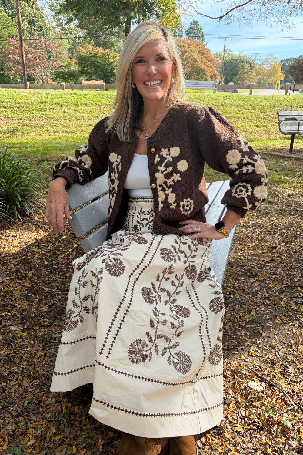 A person wearing a cream maxi skirt with brown floral embroidery and a matching brown cardigan.