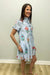 Woman wearing a floral striped dress standing against a plain wall.