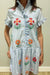 Woman wearing a dress with floral embroidery against a plain background