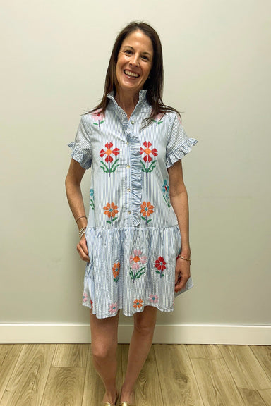 Woman wearing a floral dress standing against a plain wall.