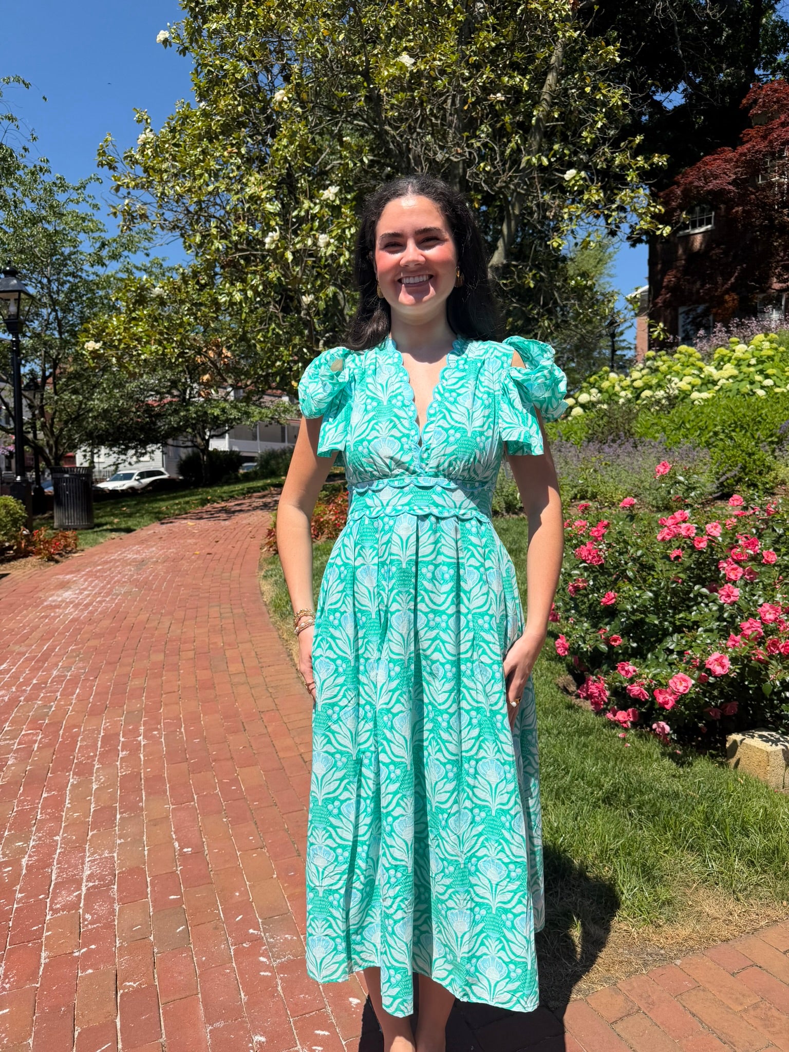 Woman in a blue dress standing outdoors with flowers and a building in the background