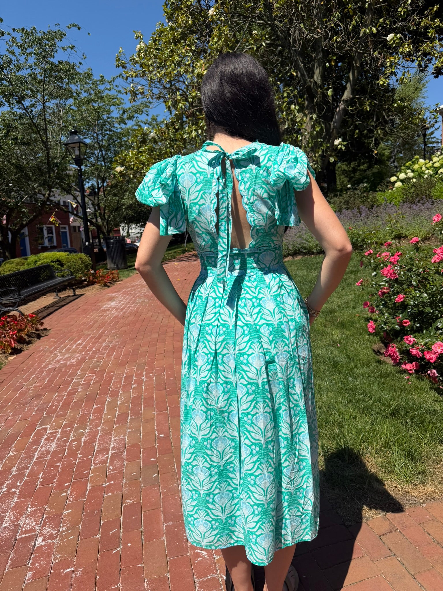 Woman in a green dress standing on a brick path with trees and flowers in the background