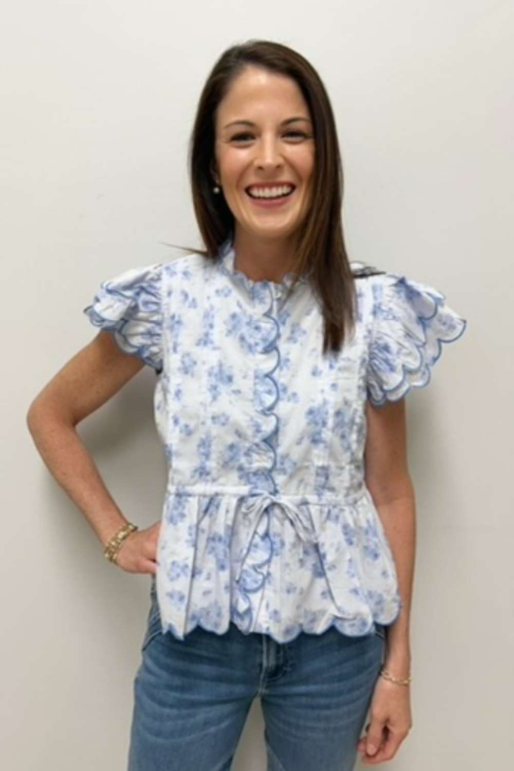 Woman wearing a blue floral blouse and jeans against a plain background