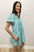 Woman wearing a teal floral dress against a white wall