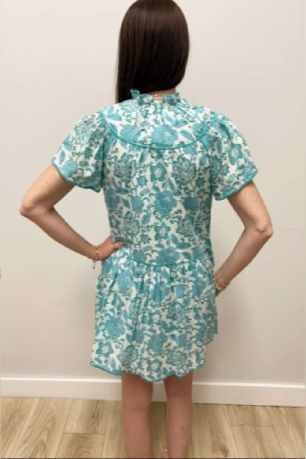 Person wearing a blue floral dress against a white wall.