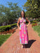 Woman in a pink floral dress standing on a brick path with trees and greenery in the background