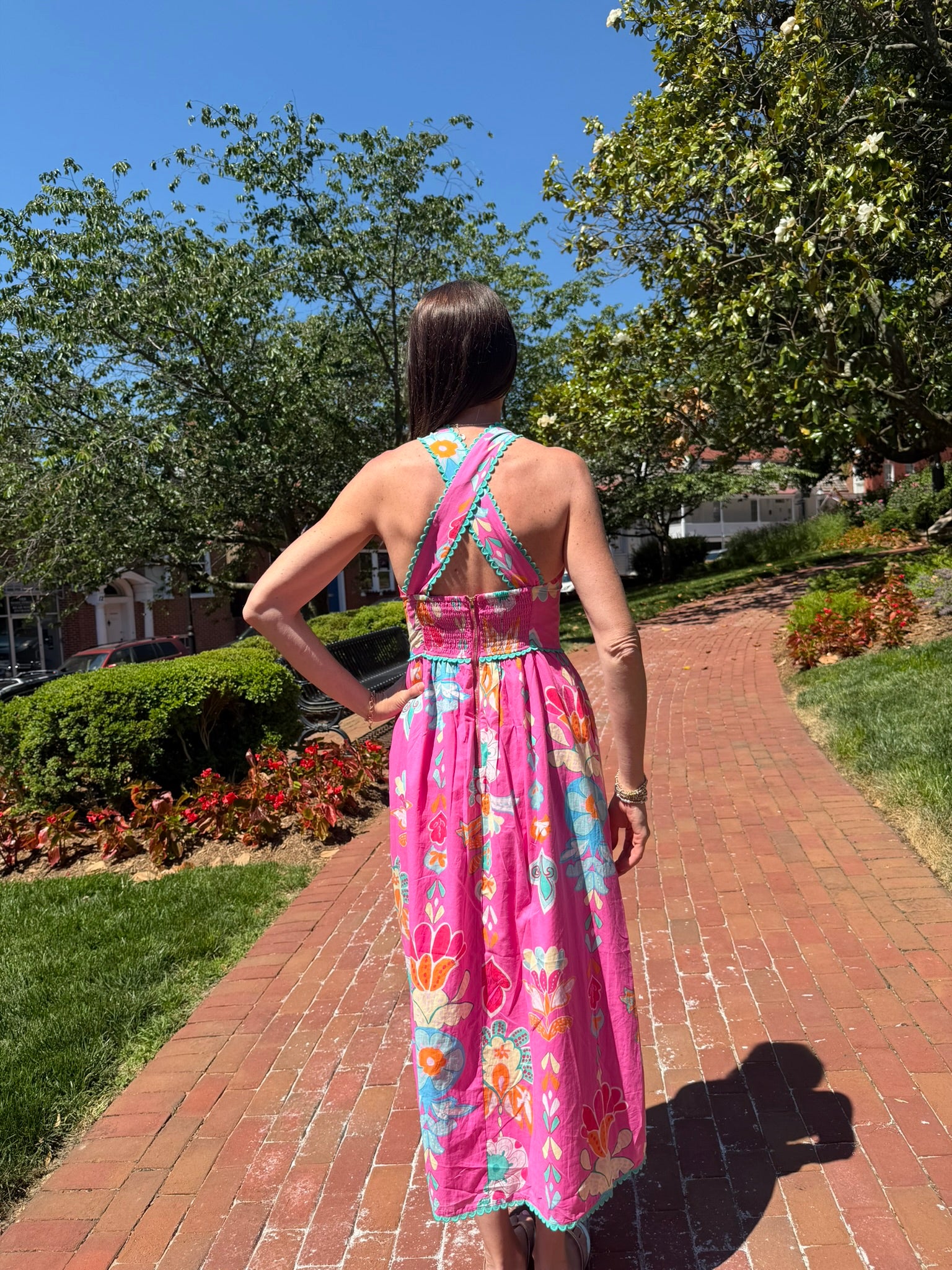 Woman in a colorful dress standing on a brick path with trees and grass in the background