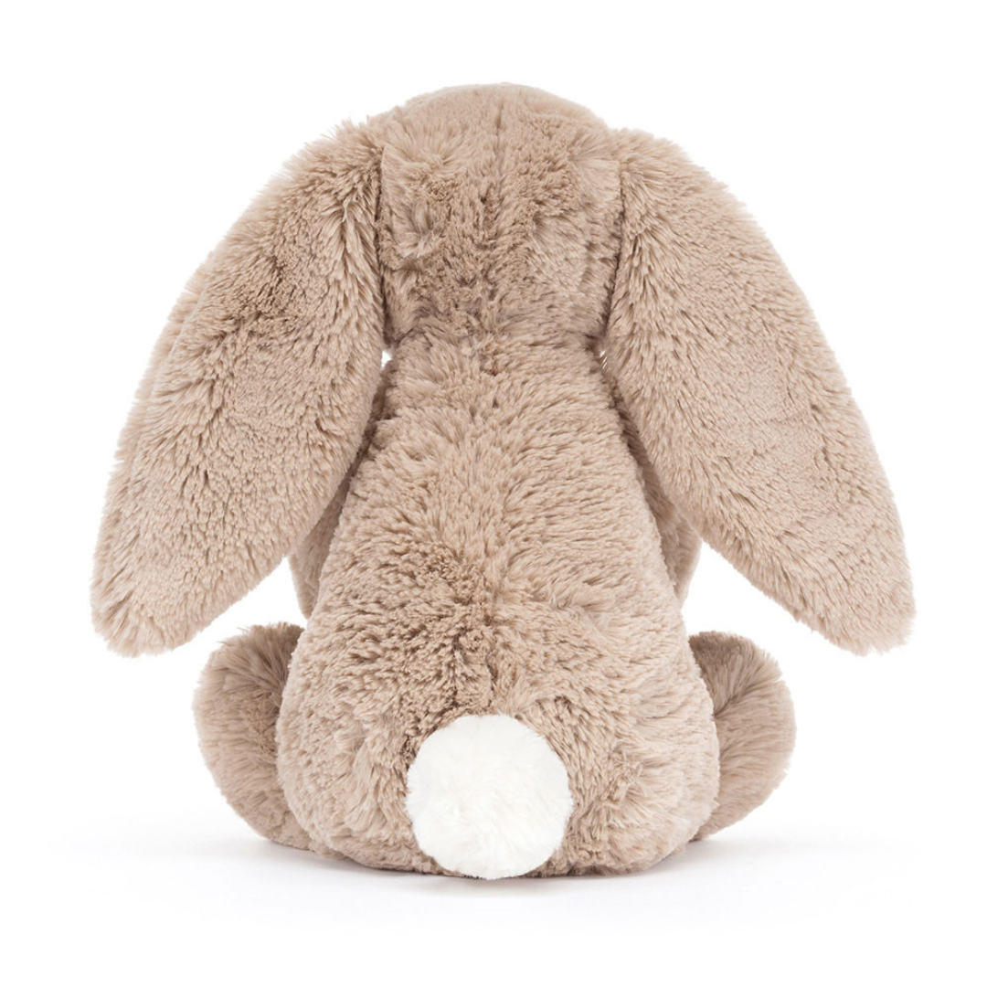 Jellycat Bashful Beige Bunny 'Birthday' is a beige plush bunny holding a plush double layer yellow cake topped with red strawberries, cream frosting, and a lit red and white striped candle. Back facing sitting