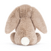 Jellycat Bashful Beige Bunny 'Birthday' is a beige plush bunny holding a plush double layer yellow cake topped with red strawberries, cream frosting, and a lit red and white striped candle. Back facing sitting
