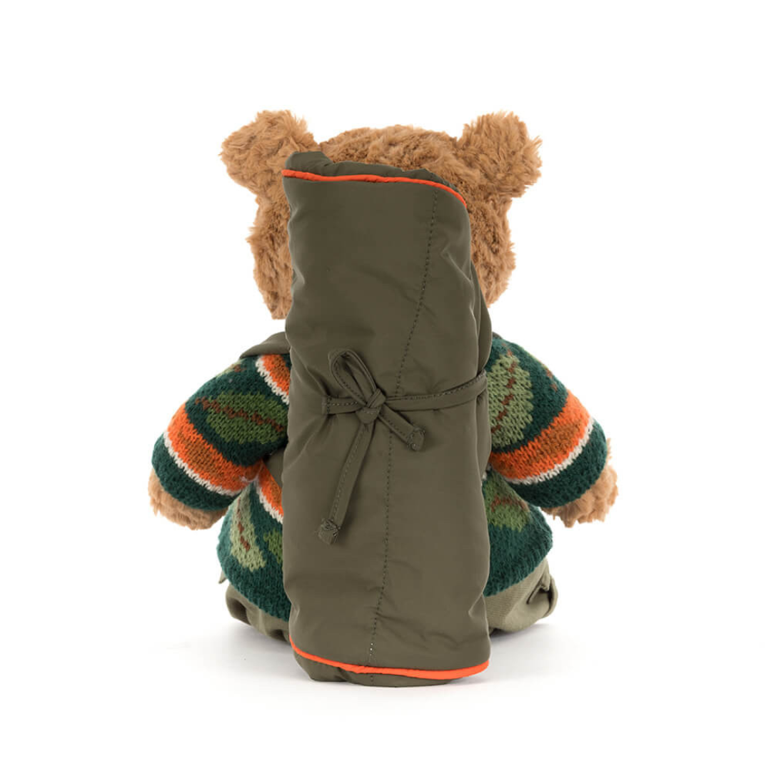 Stuffed bear wearing a green jacket with a striped sweater on a white background