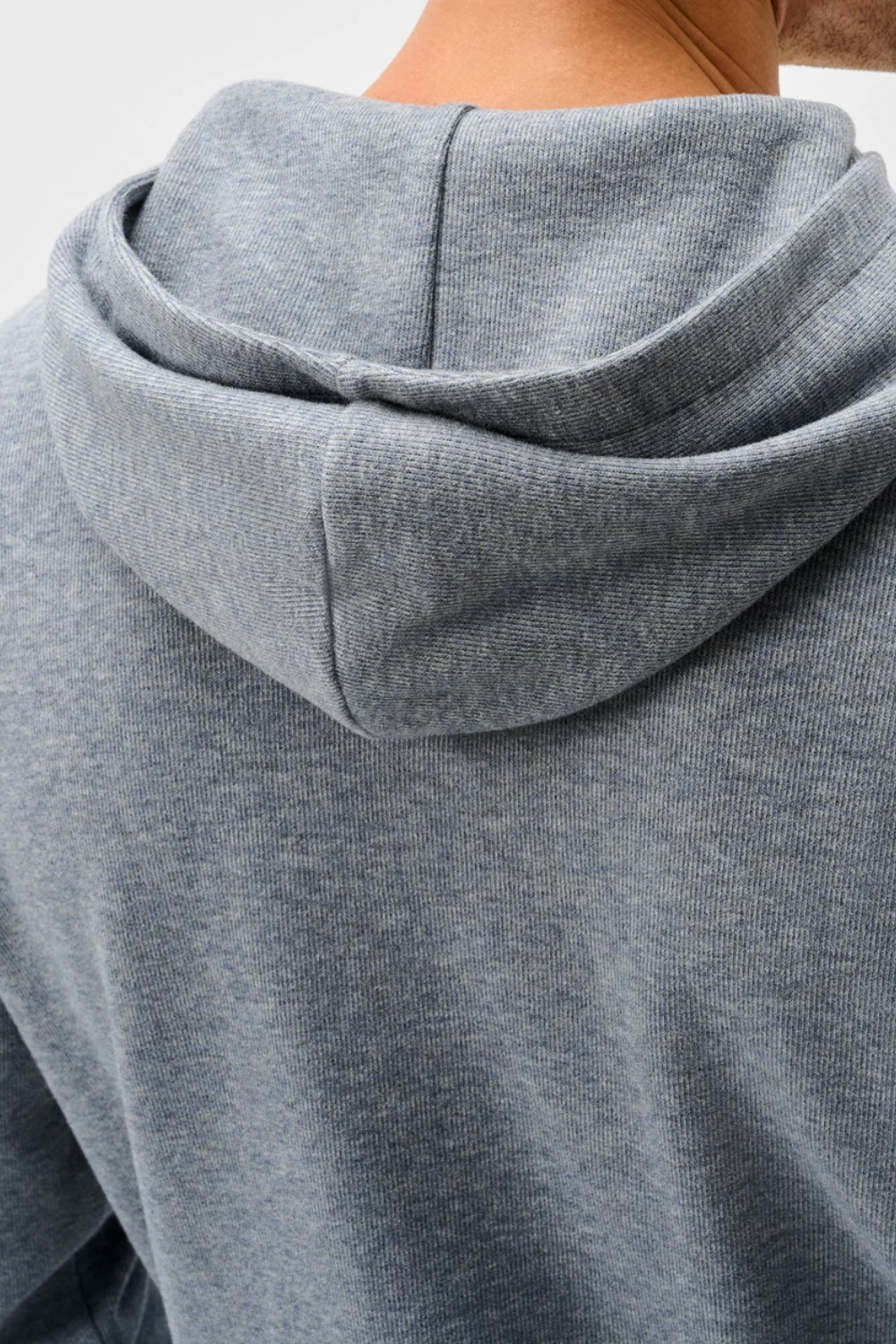 Close-up of the back of a heather gray hooded sweatshirt worn by a model, showing the hood and shoulder area.