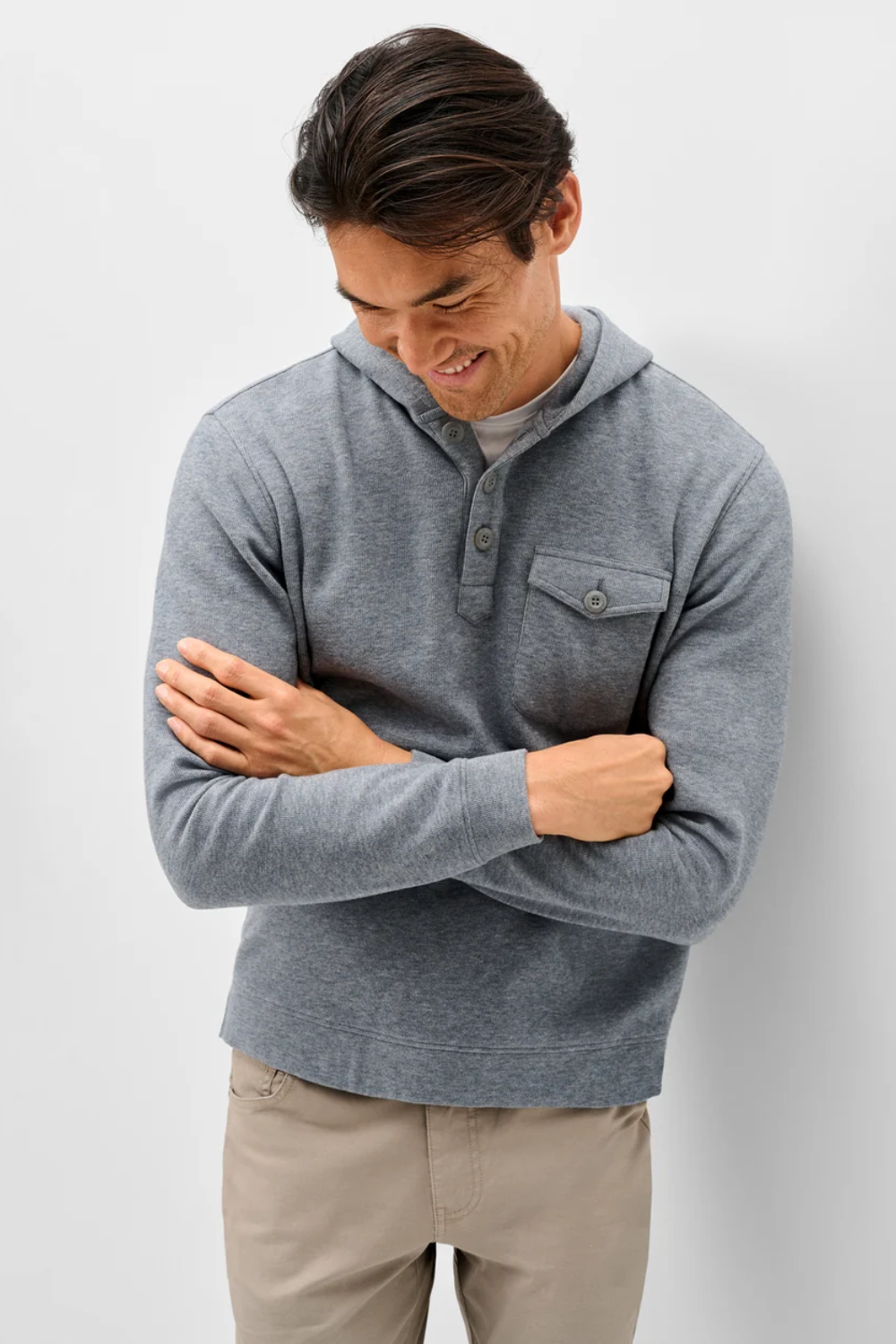 A man wearing a heather gray long-sleeve henley hoodie with a chest pocket, paired with beige pants, standing against a light gray studio background.