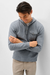 A man wearing a heather gray long-sleeve henley hoodie with a chest pocket, paired with beige pants, standing against a light gray studio background.