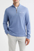A man wearing a light blue quarter-zip knit sweater with a chest pocket, paired with white pants, against a plain light gray background.