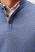 Close-up of a textured blue polo shirt with a gray inner placket and dark buttons, worn over a red and white checkered collared shirt.