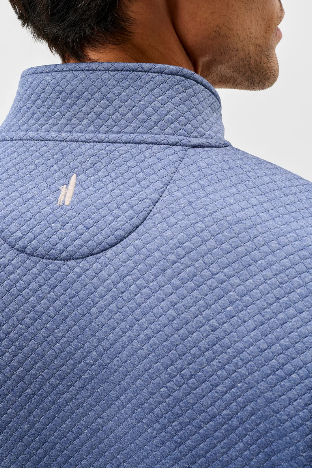 Close-up of a man wearing a textured blue quarter-zip pullover jacket, showing the back collar and a small white embroidered logo.