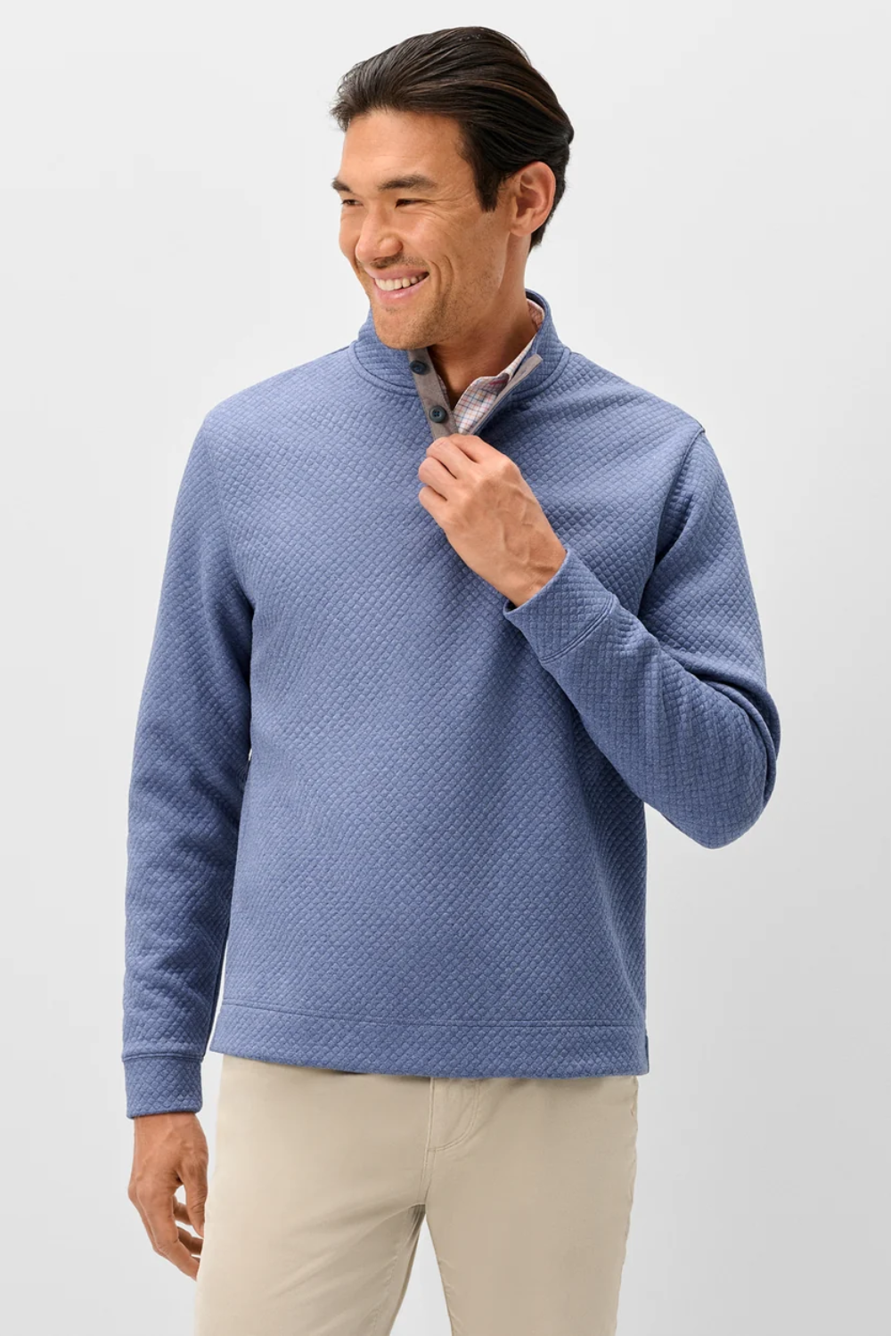 A man wearing a textured blue quarter-zip pullover sweater and beige pants, standing against a light gray studio background.