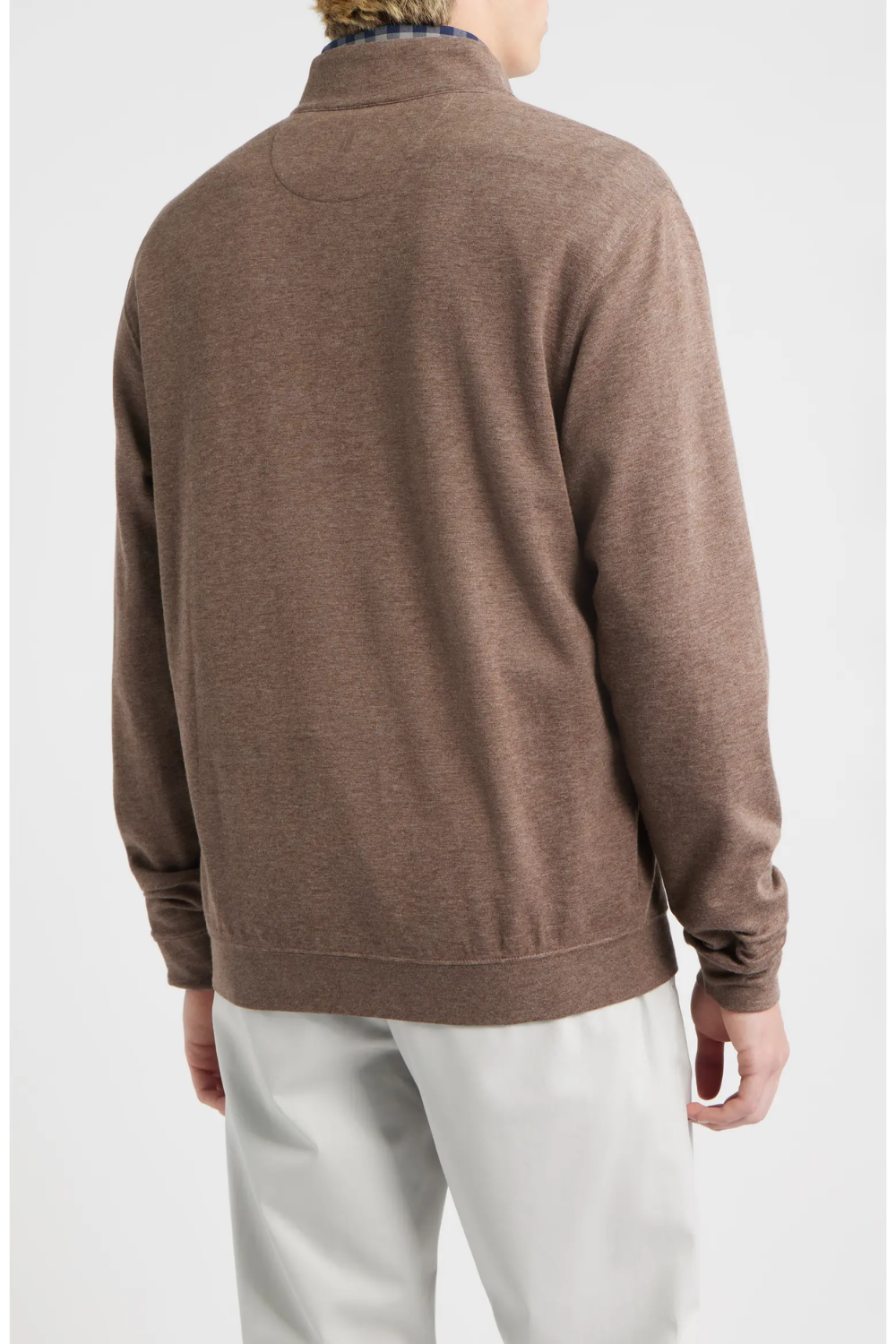 A man viewed from the back wearing a brown long-sleeve quarter-zip sweater and white trousers, against a light gray studio background.