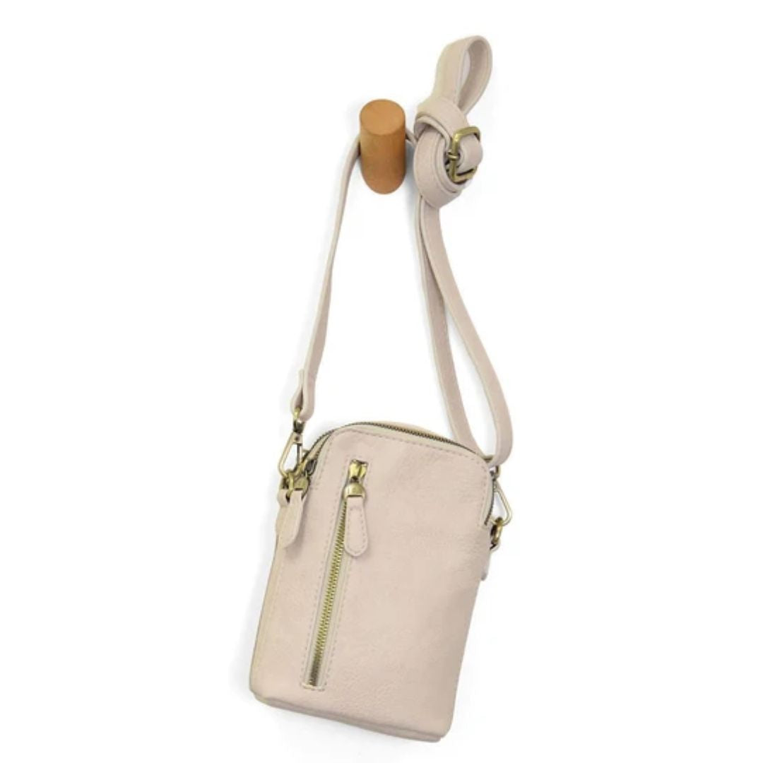 A small beige crossbody phone bag with a top zipper and a vertical zippered pocket, hanging from a wooden display stand against a white background.
