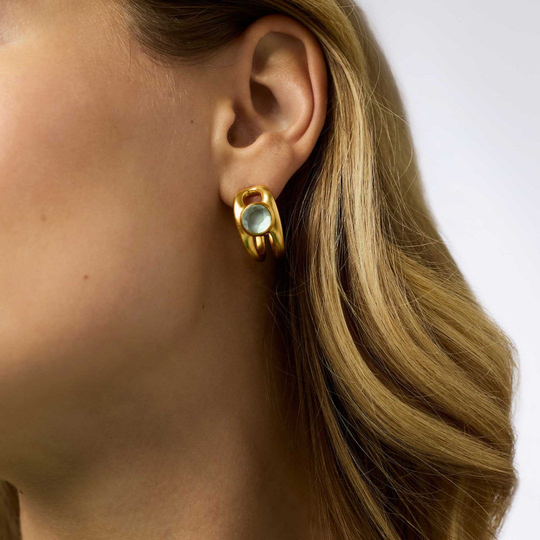 Gold earring with a gemstone worn by a person with blonde hair.