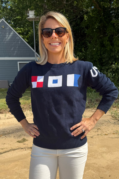 Woman wearing a navy sweater with colorful flags, standing outdoors.