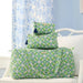 Three quilted travel or toiletry bags stacked on a white chair, featuring a green, white, and blue geometric floral pattern with dark blue tassels on the zippers.