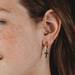 Close-up of an ear wearing a gold cross earring with a blurred background