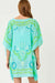 Woman wearing a turquoise cover-up with shell and leaf patterns on a white background