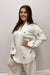 Woman wearing a white outfit with green patterns against a plain background