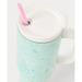 A close-up of a handled tumbler with a white lid and pink straw, featuring a mint green and white tree pattern with small pink and green leaf accents.