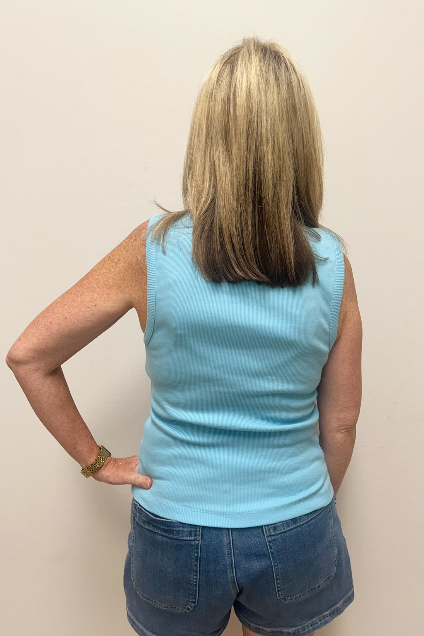 Woman wearing light blue tank top with pearl detail around the neck