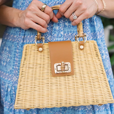 Wicker handbag with brown leather patch held by a person wearing a blue dress.