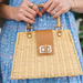 Wicker handbag with brown leather patch held by a person wearing a blue dress.