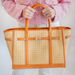 Person holding a woven handbag with orange leather trim against a white background