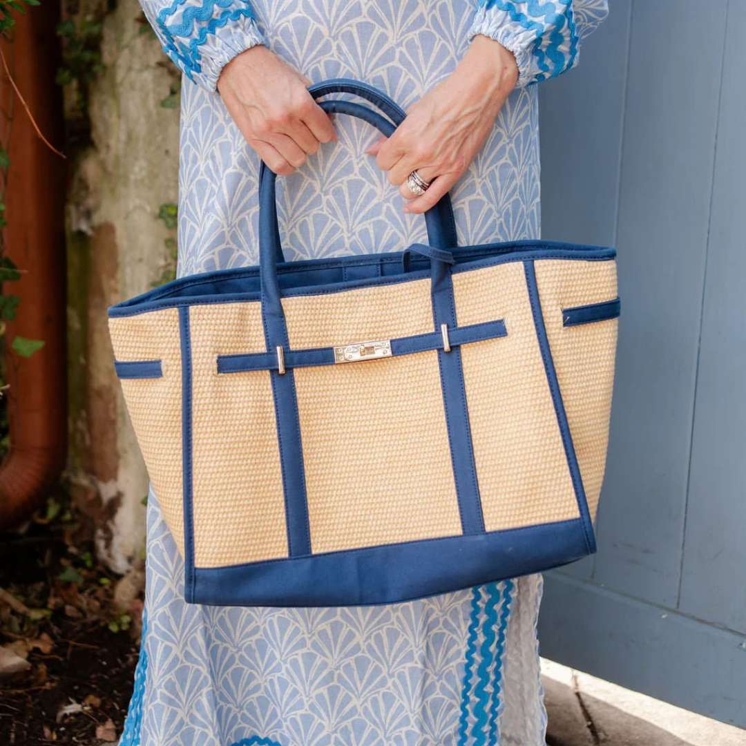 Person holding a straw tote bag with blue accents outdoors.