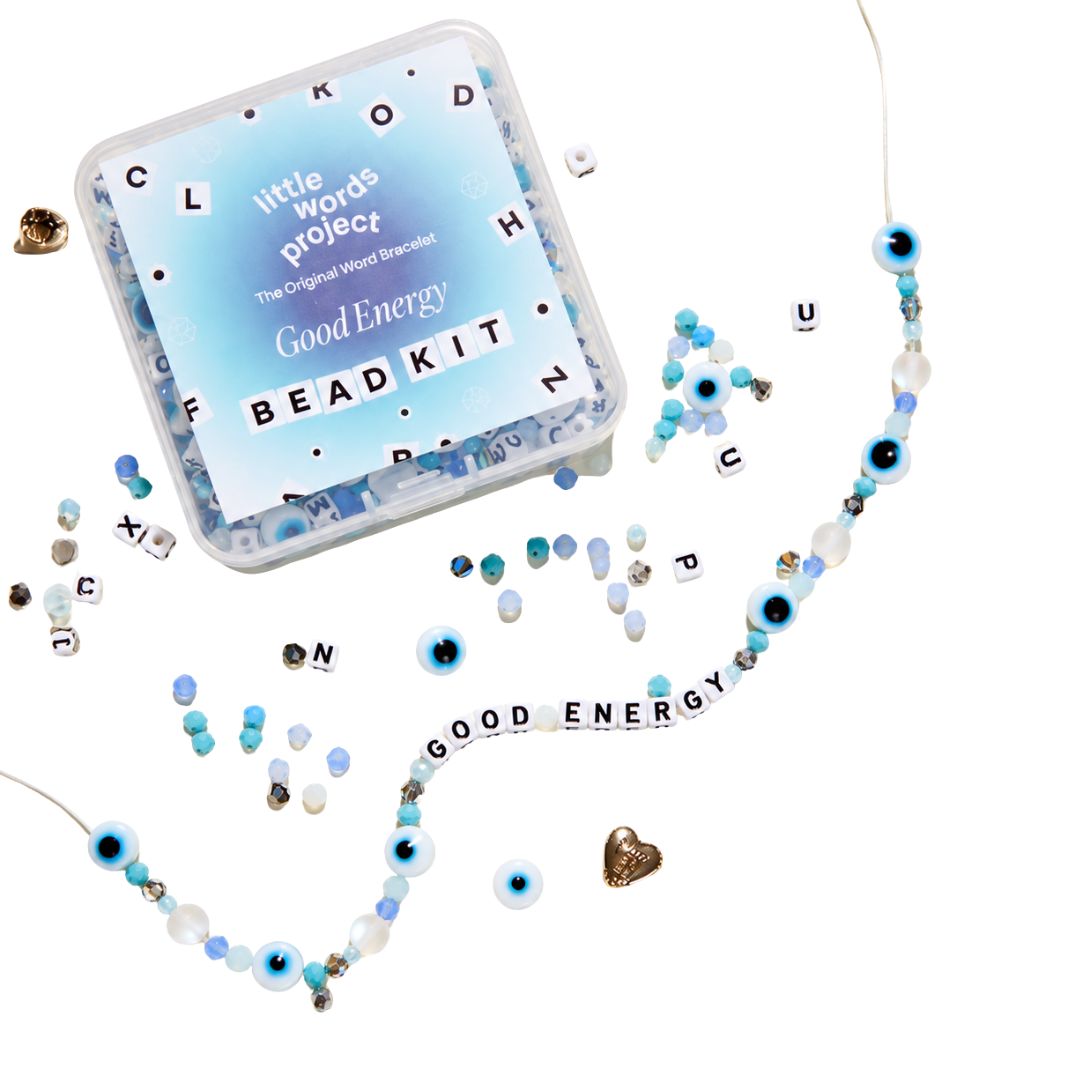 A bead kit labeled 'little words project Good Energy BEADKIT' shown with a clear plastic case and scattered beads, letter tiles, and a partially assembled word bead necklace on a white background.