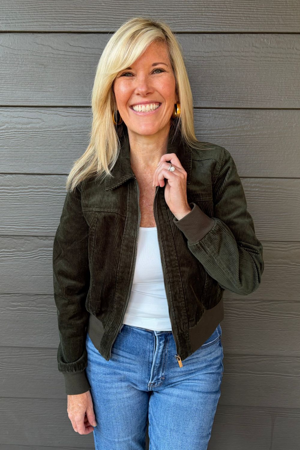 Woman wearing Liverpool Collared Bomber Jacket In Hunter Green with jeans on a dark wood background.