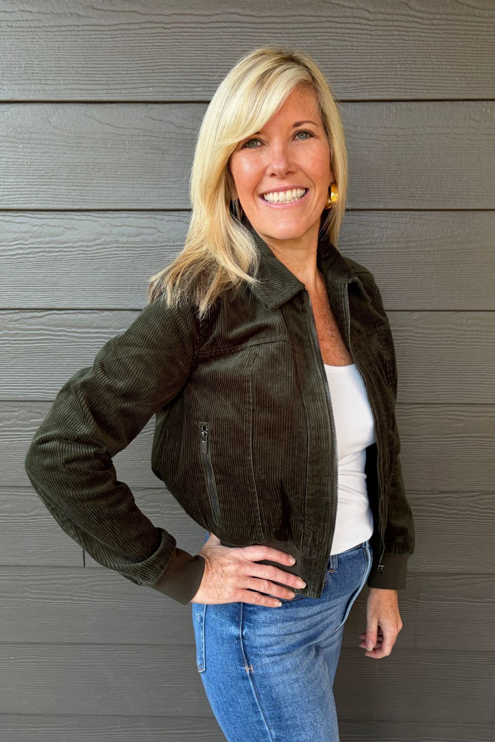 Woman wearing Liverpool Collared Bomber Jacket In Hunter Green with jeans on a dark wood background.