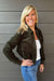 Woman wearing Liverpool Collared Bomber Jacket In Hunter Green with jeans on a dark wood background.