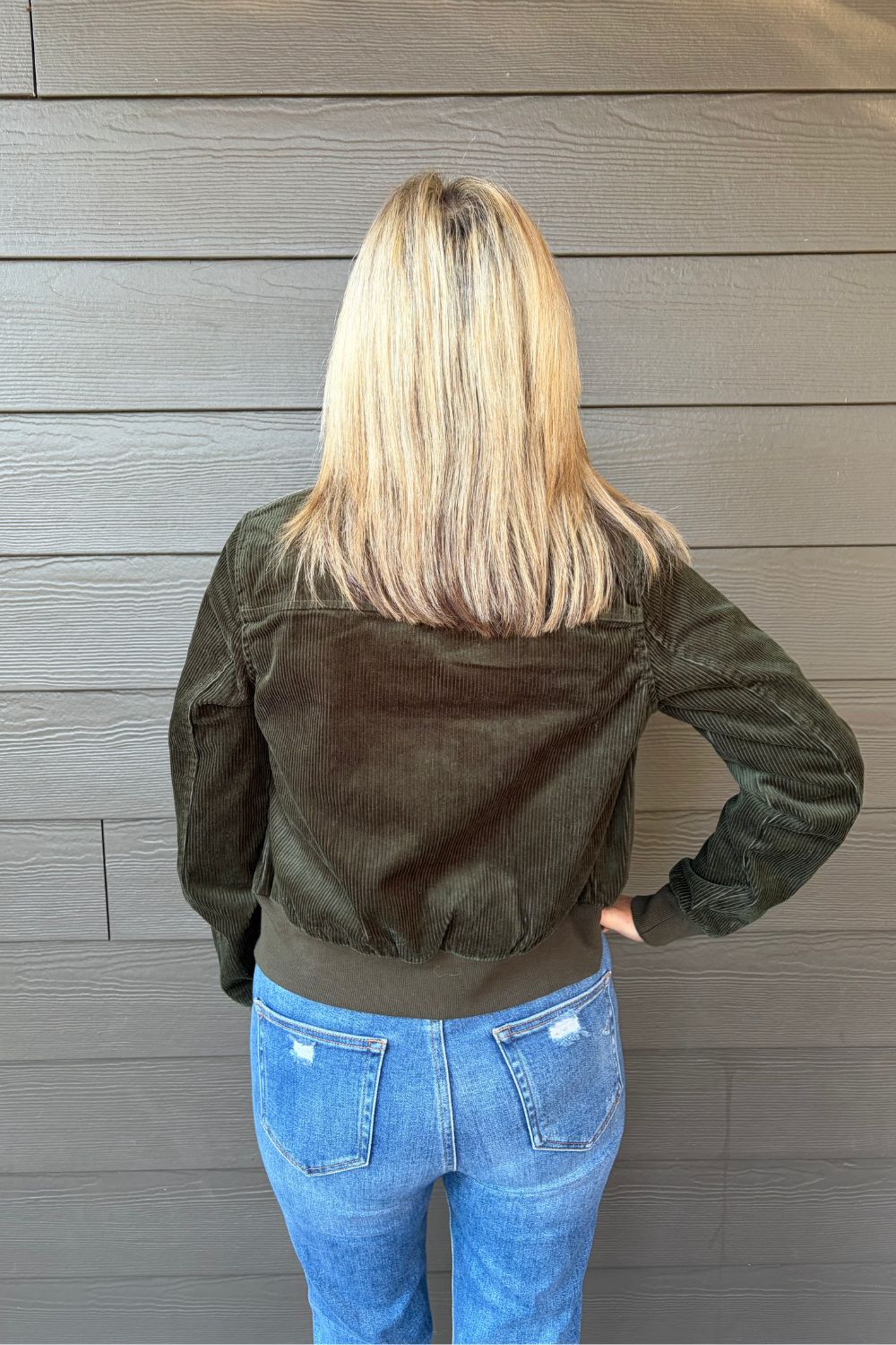 Woman wearing Liverpool Collared Bomber Jacket In Hunter Green with jeans on a dark wood background.
